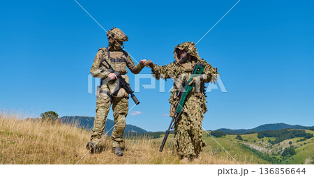 Two Soldiers in Camouflage and Ghillie Suit Fist Bumping During Mountain Training Exercise With Sniper Rifle 136856644