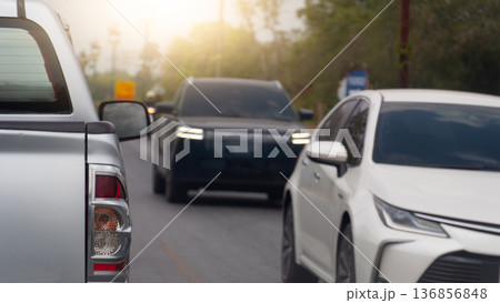 Rear side of pickup truck car driving on asphalt road. A sedan coming from the opposite direction drove past. Background blurred of trees and light shining from behind. Rear side of pickup truck car driving on asphalt road. A sedan coming from the opposite direction drove past. Background blurred of trees and light shining from behind. 136856848