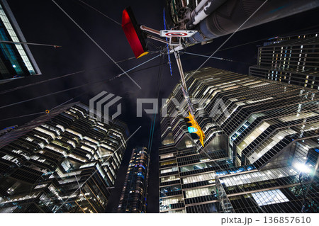 Night reflections rise into a maze of glass and steel as a glowing traffic light hangs beneath towering skyscrapers. The scene feels like a futuristic canyon where geometry, light 136857610