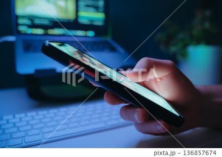 Close up of hand browsing content on a mobile phone in front of a desk 136857674