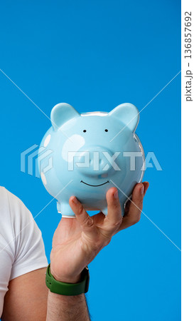 Holding a blue piggy bank with a simple smile against a bright blue background 136857692