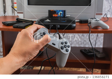 Passion for computer and console games. The process of playing games in a home environment. Hand holding a game controller Passion for computer and console games. The process of playing games in a home environment. Hand holding a game controller 136858271