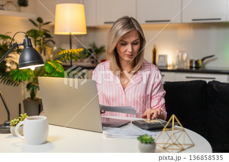 Adult woman with laptop and calculator tracks budget marks bills paid notes savings manages expenses Adult woman with laptop and calculator tracks budget marks bills paid notes savings manages expenses 136858535