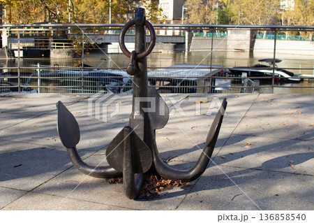 Large metal anchor displayed near a river in a city park during autumn 136858540