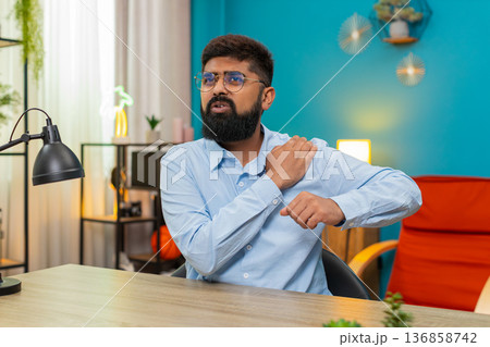 Indian man clutching painful shoulder injury sharp discomfort strained muscle seeking relief indoors Indian man clutching painful shoulder injury sharp discomfort strained muscle seeking relief indoors 136858742