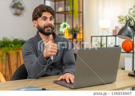 Indian man gets email partnership confirmation on laptop smiles thumbs up celebrates win happy news Indian man gets email partnership confirmation on laptop smiles thumbs up celebrates win happy news 136858807