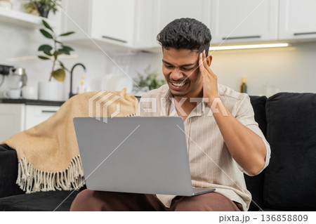 Indian man squints at laptop screen rubs temples does breath exercise then returns to focused work Indian man squints at laptop screen rubs temples does breath exercise then returns to focused work 136858809