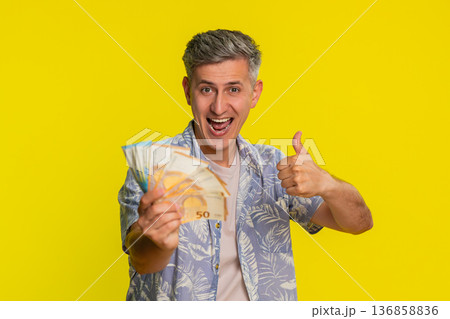 Adult man jumping with joy waving and holding euro cash celebrating win in lottery game or jackpot Adult man jumping with joy waving and holding euro cash celebrating win in lottery game or jackpot 136858836