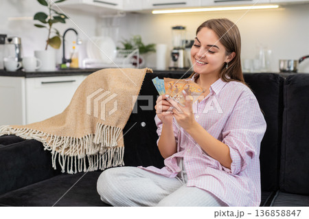 Young woman counts cash euros smiles about salary savings bonus plans dream purchase and investments Young woman counts cash euros smiles about salary savings bonus plans dream purchase and investments 136858847