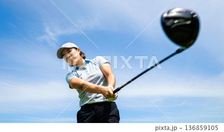 青空を背にゴルフのスイングをする女性 ドライバーショット スポーツ 爽快感 ライフスタイル 素材 136859105