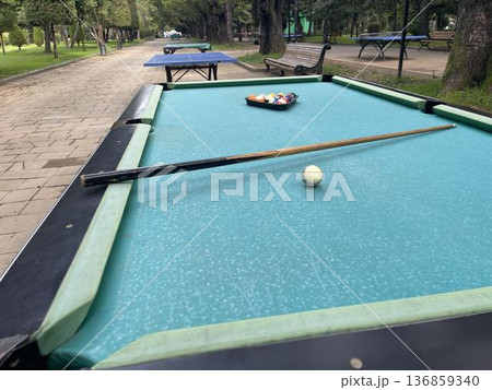 A pool table with balls and a cue in a city amusement park A pool table with balls and a cue in a city amusement park 136859340