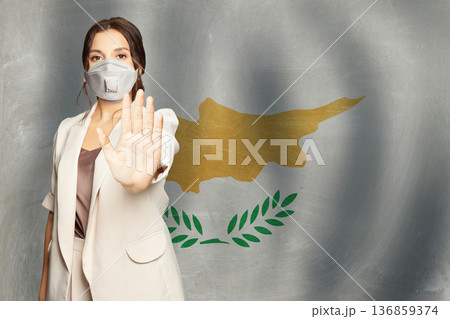 Confident woman in medical mask showing stop gesture open palm hand against Cyprus background 136859374