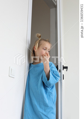 Little child girl stands at white open door and eats tangerine at home 136859431