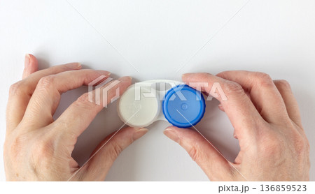 Woman's hands holding a contact lens case. Empty white plastic lens case with compartments for storing contact lenses Woman's hands holding a contact lens case. Empty white plastic lens case with compartments for storing contact lenses 136859523