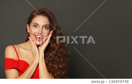 Laughing surprised woman with curly hairstyle and makeup holding her hand with her face  136859748