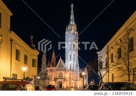 Night view of Fisherman Bastion and church in Budapest's castle district. Illuminated architecture, cobblestone streets, and historic buildings create a picturesque scene. Night view of Fisherman Bastion and church in Budapest's castle district. Illuminated architecture, cobblestone streets, and historic buildings create a picturesque scene. 136859914