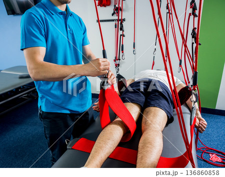 Physiotherapy. Suspension training therapy. Young man doing fitness traction Physiotherapy. Suspension training therapy. Young man doing fitness traction 136860858
