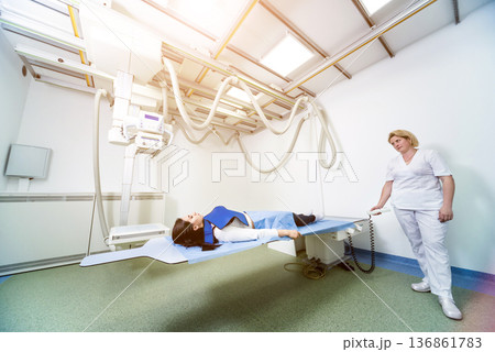 Radiologist and patient in a x-ray room. Classic ceiling-mounted x-ray system. 136861783