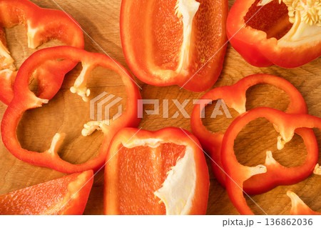 Sliced pieces, parts, lobes of sweet pepper, red, scattered on a wooden board Sliced pieces, parts, lobes of sweet pepper, red, scattered on a wooden board 136862036