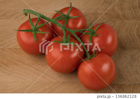 Five red tomatoes on a green branch on a wooden background. 136862128