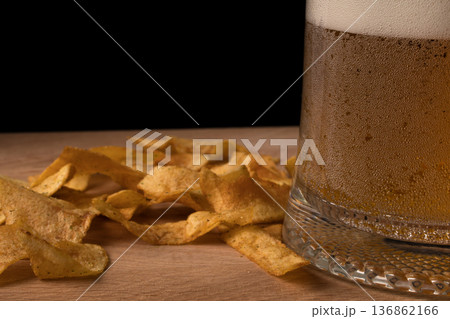 Glass with beer and chips on wood board and black background 136862166