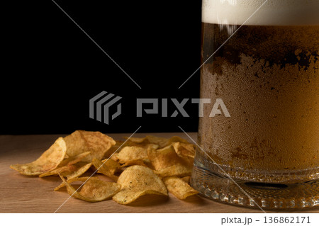 Glass with beer and chips on wood board and black background Glass with beer and chips on wood board and black background 136862171