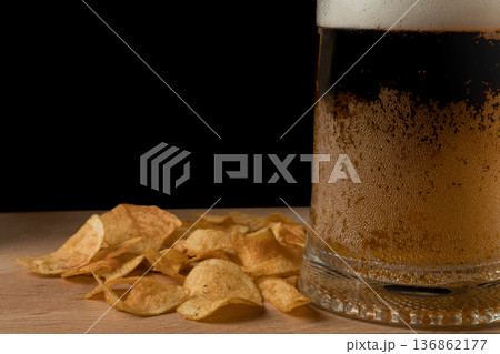 Glass with beer and chips on wood board and black background Glass with beer and chips on wood board and black background 136862177