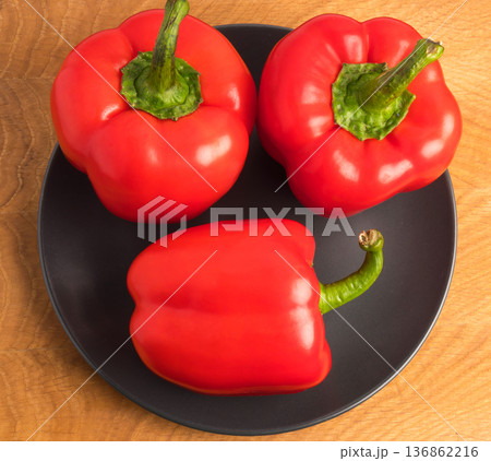 Three sweet peppers in a black plate on a wooden board Three sweet peppers in a black plate on a wooden board 136862216