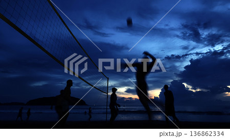 Young people playing beach volleyball by the ocean at sunset Young people playing beach volleyball by the ocean at sunset 136862334