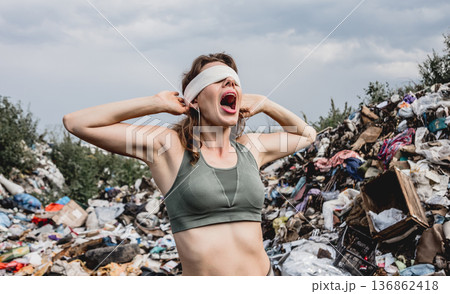 A blindfolded female volunteer screams from powerlessness in a dump of plastic rubbish. A blindfolded female volunteer screams from powerlessness in a dump of plastic rubbish. 136862418