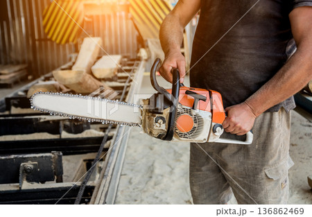 Woodcutter cutting tree with chainsaw on sawmill. Woodcutter cutting tree with chainsaw on sawmill. 136862469