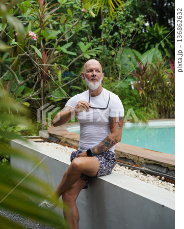 A man is comfortably sitting near a swimming pool in tropical area A man is comfortably sitting near a swimming pool in tropical area 136862632