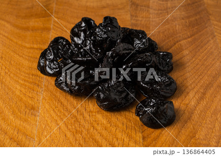 Dried dried prunes in a heap on a wooden board 136864405