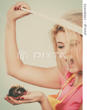 Woman holding cupcake wearing colander on head Woman holding cupcake wearing colander on head 136864458