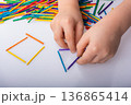 Kid making geometric shapes with colorful sticks on white background 136865414