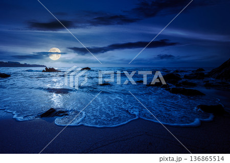 beautiful empty sandy beach at the sea at night. white foam rolling on to the shore near boulder in full moon light. perfect summer vacation concept. awesome weekend mysterious fantasy. low angle beautiful empty sandy beach at the sea at night. white foam rolling on to the shore near boulder in full moon light. perfect summer vacation concept. awesome weekend mysterious fantasy. low angle 136865514