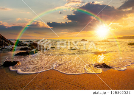beautiful sunset over empty sandy beach at the sea. white foam rolling on to the shore near boulder in evening light with rainbow. perfect summer vacation concept. awesome weekend. low angle view 136865522