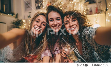 Friends gen-z enjoy drinks together at a cozy gathering during evening hours with warm lights 136865599