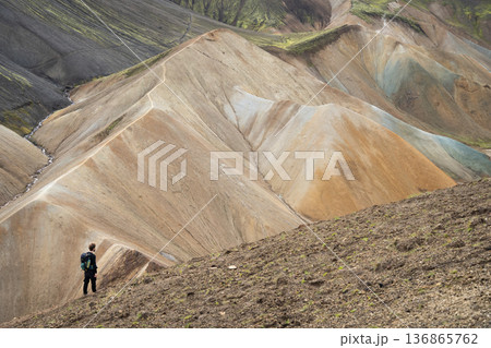 Hiker on a ridge looking on colorful mountains and ridges in front of him, Highlands, Iceland 136865762