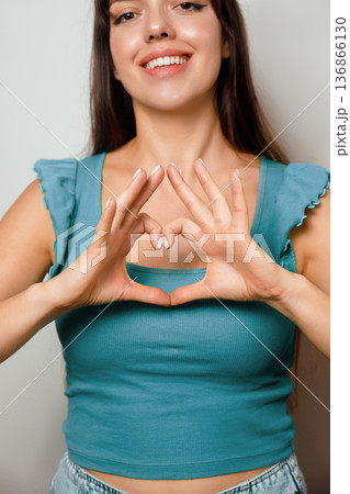 Woman making a heart shape with her hands, smiling at the camera in a bright indoor setting during daytime Woman making a heart shape with her hands, smiling at the camera in a bright indoor setting during daytime 136866130