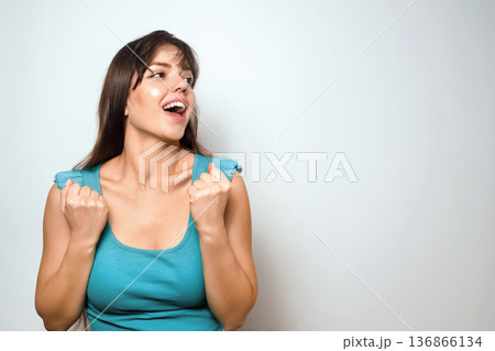 Woman shows excitement and joy while standing against a plain background during a casual indoor setting Woman shows excitement and joy while standing against a plain background during a casual indoor setting 136866134