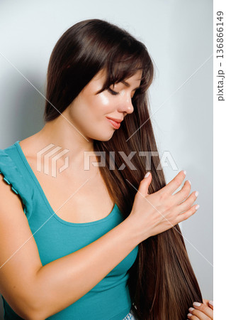 Woman with long hair touches her hair and poses in a studio setting with white wall background Woman with long hair touches her hair and poses in a studio setting with white wall background 136866149