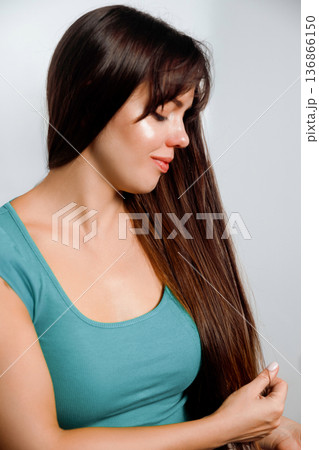 Woman with long hair looking down while touching her hair in a simple setting Woman with long hair looking down while touching her hair in a simple setting 136866150