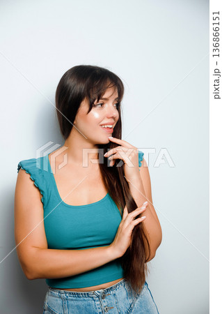 Woman smiles and looks to the side while posing in a studio setting with a plain background 136866151