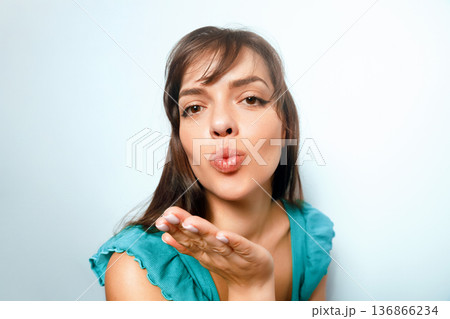 Woman blowing a kiss with a light blue background while wearing a blue top, showcasing a cheerful expression 136866234
