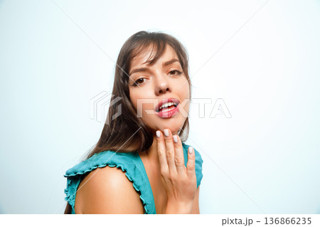 Woman smiles and poses while touching her cheek in a studio setting with light background during daytime Woman smiles and poses while touching her cheek in a studio setting with light background during daytime 136866235