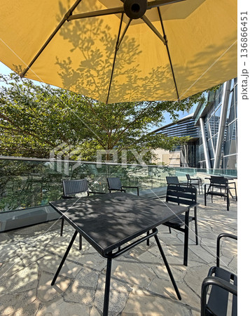 Outdoor cafe seating with yellow umbrella casting tree shadows on tables and chairs 136866451