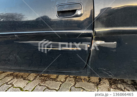 Scratched black car door with visible paint damage and rust marks close up of vehicle body after minor accident outdoors. 136866465