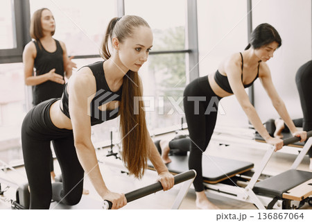 Focus on woman with pony tail. Three young fit women training in gym with a female trainer. Women wearing black sportwears. Focus on woman with pony tail. Three young fit women training in gym with a female trainer. Women wearing black sportwears. 136867064