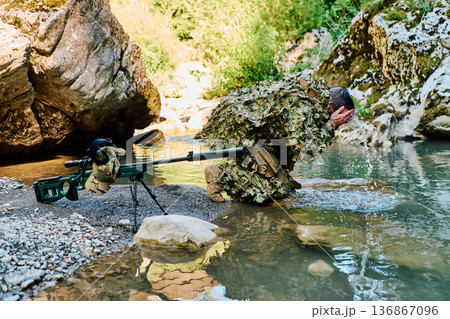Camouflaged Sniper Soldier Washing Face Beside River With Precision Rifle in Rocky Gorge Camouflaged Sniper Soldier Washing Face Beside River With Precision Rifle in Rocky Gorge 136867096